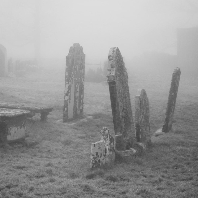 Atmospheric black and white photo of leaning gravestones in the mist.
