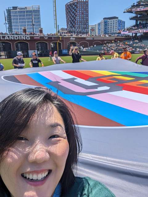 Photo of Joy and a large SF Giants pride flag on the field at Oracle Park in San Francisco with others chosen to hold the flag.