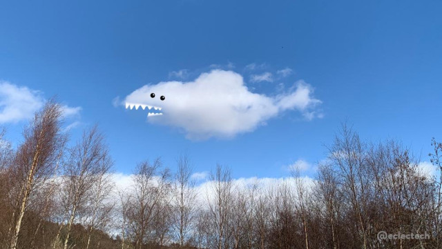 Photo of a blue sky with white fluffy clouds, and a row of tree tops across the bottom. There is one main cloud shaped very much like a shark, so I have added eyes and pointy teeth.