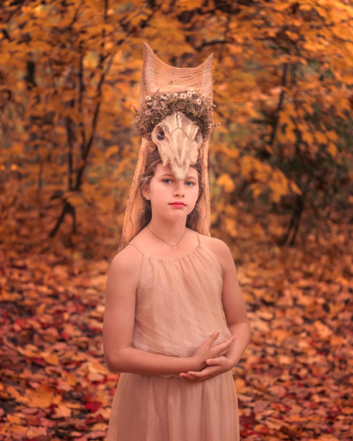 Girl in a yellow wood. She is wearing a cream dress and an elaborate headpiece made out of an animal skull.