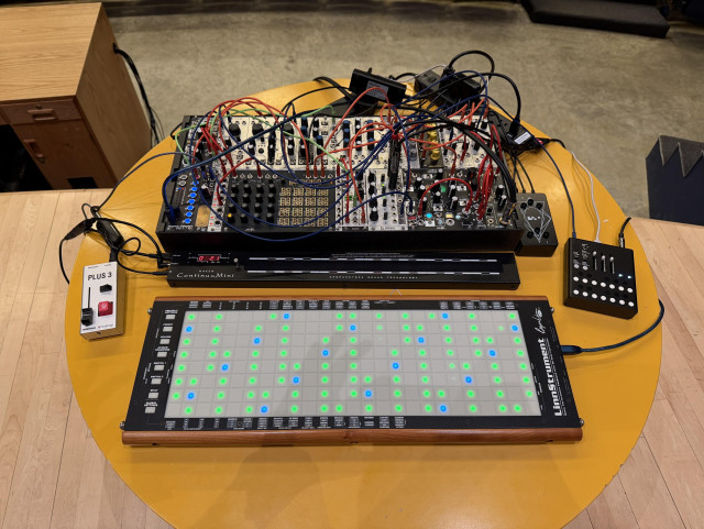 Moderately large and heavily patched synth setup on a very ugly yellow circular table.
