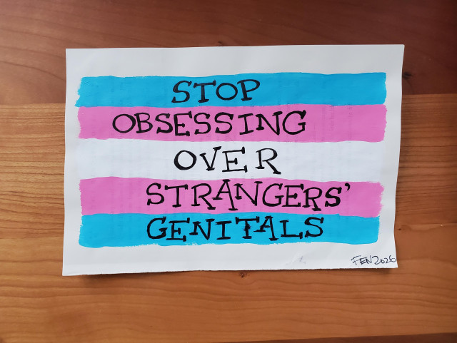 A trans flag painted on pages torn from a harry potter book. Written on top in the harry potter font are the words 'Stop Obsessing over strangers' genitals'.