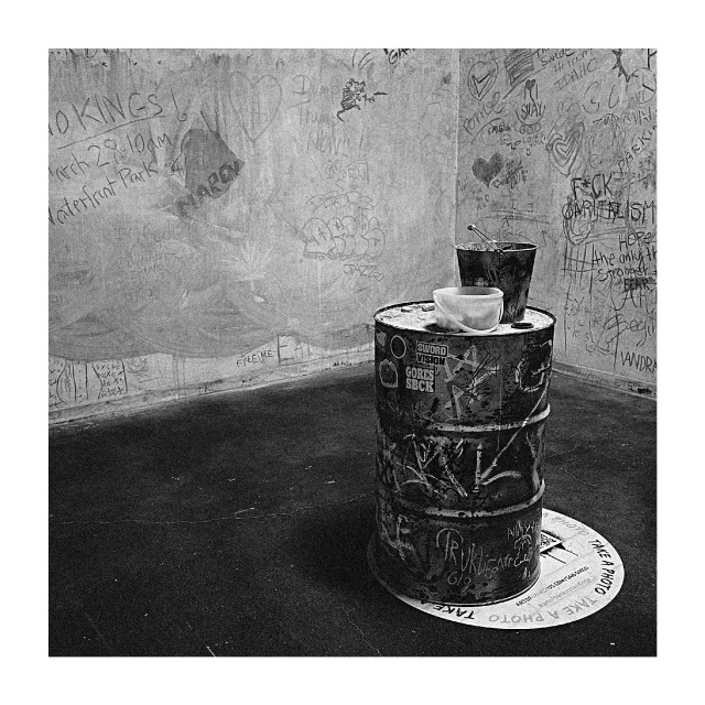 A graffiti-covered room centers on a chalk-covered barrel topped with cups and a bucket.