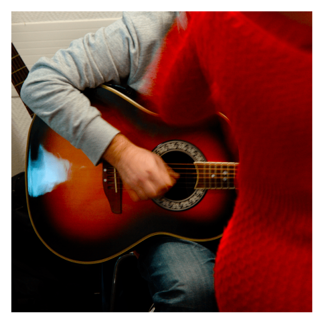 Square format indoor photography.

A guitar laying on a leg while being pinched, half of an inhabited red dress occupying the right side.