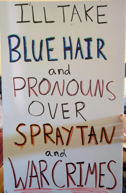 A protest sign that says "I'll take blue hair and pronouns over spray tan and war crimes" in all caps (except for the two "and"s).

"blue hair" is shadowed in blue, "pronouns" in pink, "spray tan" in dripping orange, and "war crimes" in red.