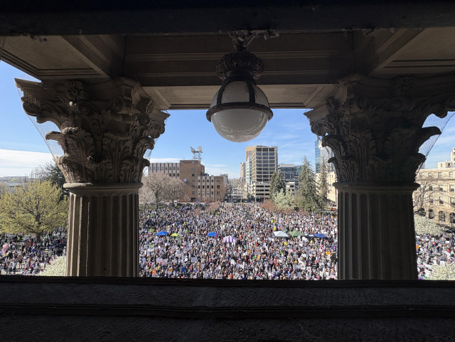 View is of a large crowd as seen through the columns of the Capitol. 