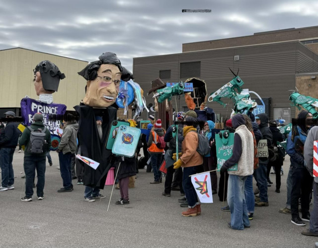 Photo of protesters assembling to march , with oversized puppet heads of Prince and RGB, and a row of locust puppets