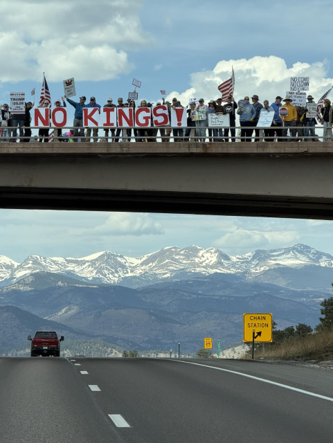 No kings protest on a bridge with mountains in the background. 