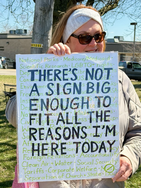 A No Kings protester with a sign saying, “There’s not assigned big enough to fit all the reasons I’m here today,” with a bunch of reasons in small type behind the large print.