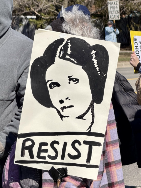 A No Kings protester with a sign with a black and white graphic image of princess Leah from Star Wars saying, “RESIST”.