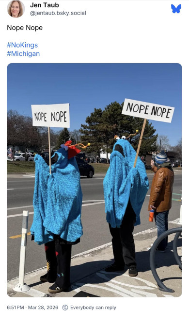 Two people dressed up as Sesame Street blue Martians carrying signs that say, “Nope nope”
