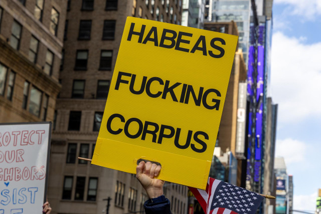 A yellow protest sign with the words “Habeas Fucking Corpus” printed on it in black block letters.
