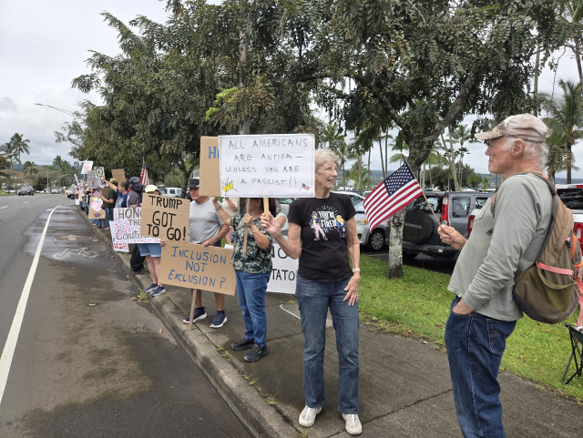 Line of protesters holding signs along a tree-lined street.  The most visible sign reads, "All Americans are antifa unless you are a fascist."