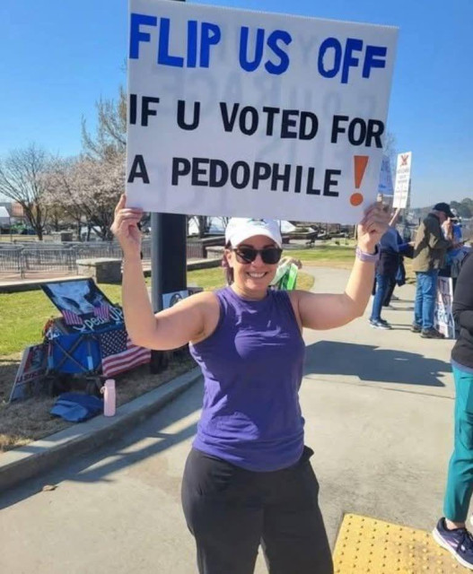 Person holding sign thas says FLIP US OFF IF U VOTED FOR A PEDOPHILE!