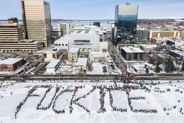 Photo of protest in downtown Anchorage, Alaska. Beautiful day. People set up on the snowy park strip spelling out FUCK ICE 