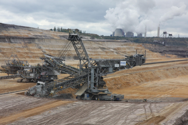 A coal digging machine with a coal power plant in the background