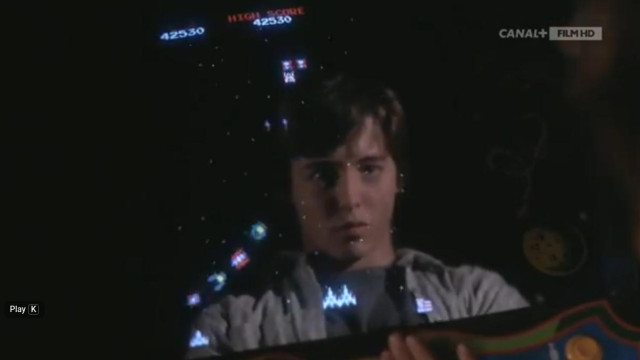 Screenshot from the movie showing a reflection of David Lightman (Matthew Broderick) in the game console. The game console shows the user's ship and the enemy ships firing missiles.