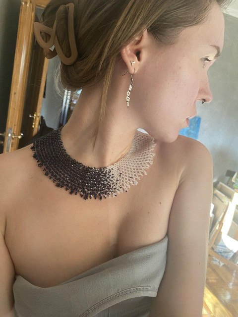 A woman wearing a strapless gray dress, a gradient beaded choker necklace, and dangling earrings, with her hair pinned up by a large clip.
