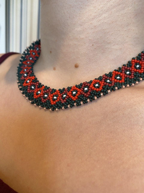 Close-up of a neck wearing a handmade beaded choker with a red and dark green geometric pattern.
