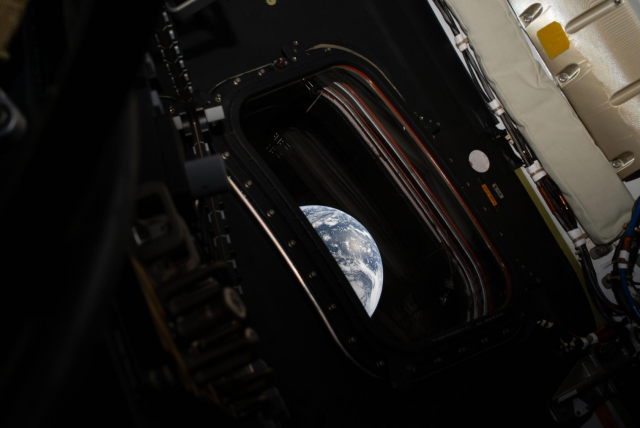 Image description by NASA on X:

One-third of Earth peeking through the window of the Orion capsule. The planet is a dreamy pale blue, swirling with white clouds and reflected sunlight. Although Earth only fills a fraction of the image it is the brightest object in the image by far. The capsule window is surrounded by a thick frame held in place with bolts, reminiscent of a heavy duty airplane window. It is dark in the capsule, but the outlines of straps and various components of the capsule are visible. Brighter white components are visible in the upper right corner.
Credit: NASA/Reid Weisman