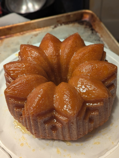 a orangey-brown bundt cake with an ornate flower shape, glistening with syrup.