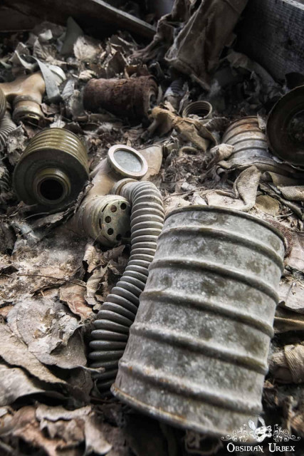 Decaying Soviet-era gas masks and filters lie scattered on a debris-filled floor in an abandoned location