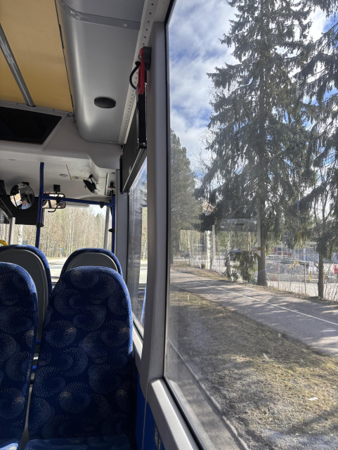 Näkymä bussin ikkunasta: puita ja tehdasalueen aita.