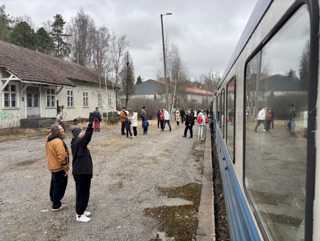Näkymä junan ovelta. Vanha asemarakennus ja ihmisiä sen edessä.
