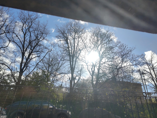 photo of some trees, houses and cars in a Glasgow street with a relatively blue sky, a few white clouds and a shiny sun