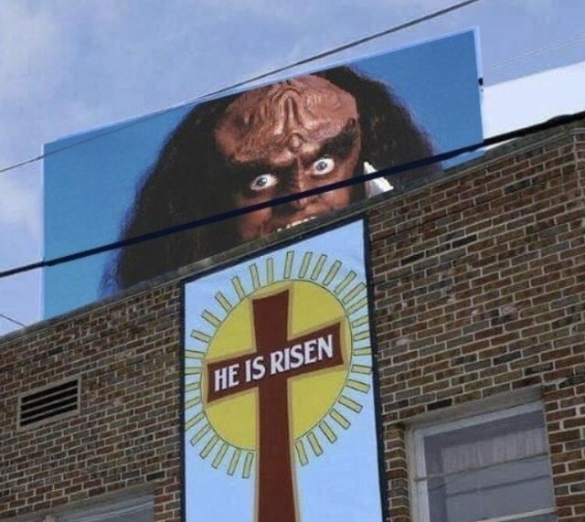 Gowron, bulging eyes & all, looms on a billboard over a building. A sign on the building with a crucifix reads, "He is risen."