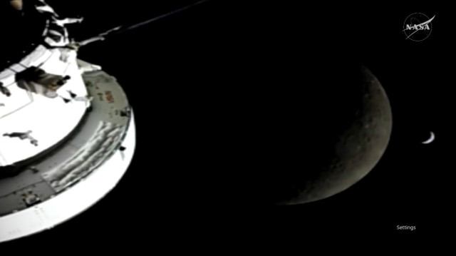 Image showing the Orion spacecraft on the left, the Moon at the center, and a crescent Earth to the right of the Moon.
