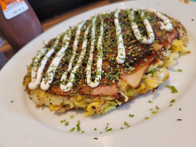 A vegan okinomiyaki on a plate ready to be served, from a different angle