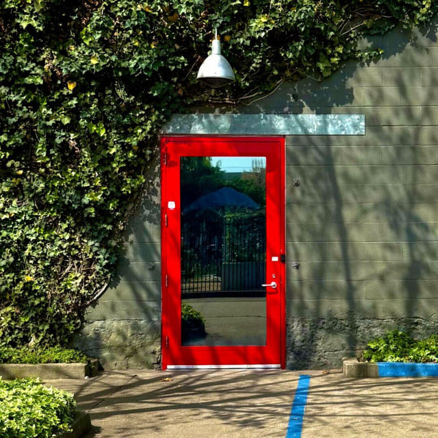 Glass door with a red frame on a grey wall that is partially covered in ivy.