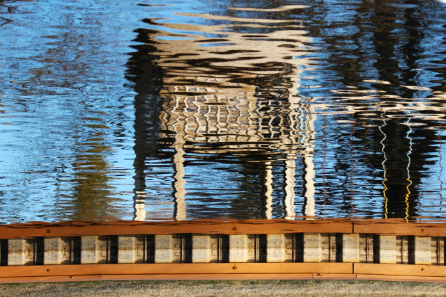 Photograph of a small children's playhouse on posts reflected in a lake and flipped upside-down.