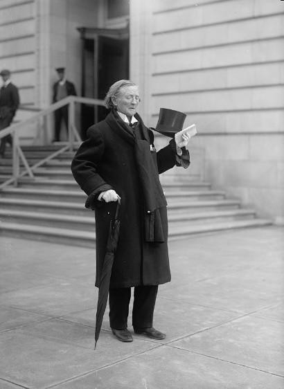 Dr Mary Edwards Walker in later life. She is wearing a trouser suit, overcoat and scarf, and carrying a top hat. She is a white woman with white hair.
