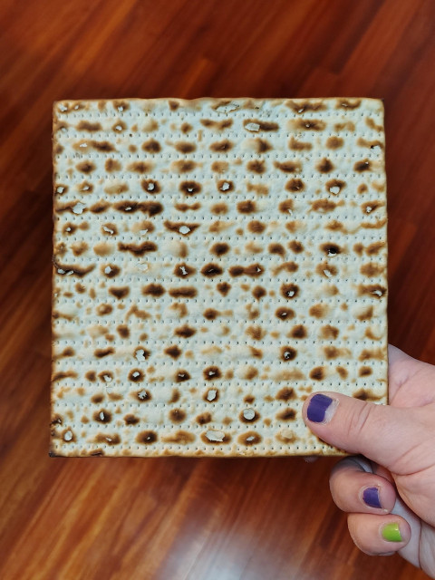 Photo of a square speckled board of matzah being held by the Undersigned.