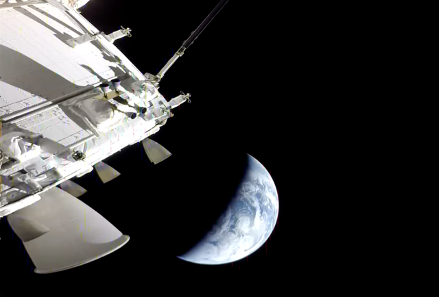 A look at Earth, a nearly half-full crescent, from one of Artemis's exterior cameras, with Artemis 2 also partially visible in the frame, most particularly part of the thruster pack, along with some exterior sensors and antennae