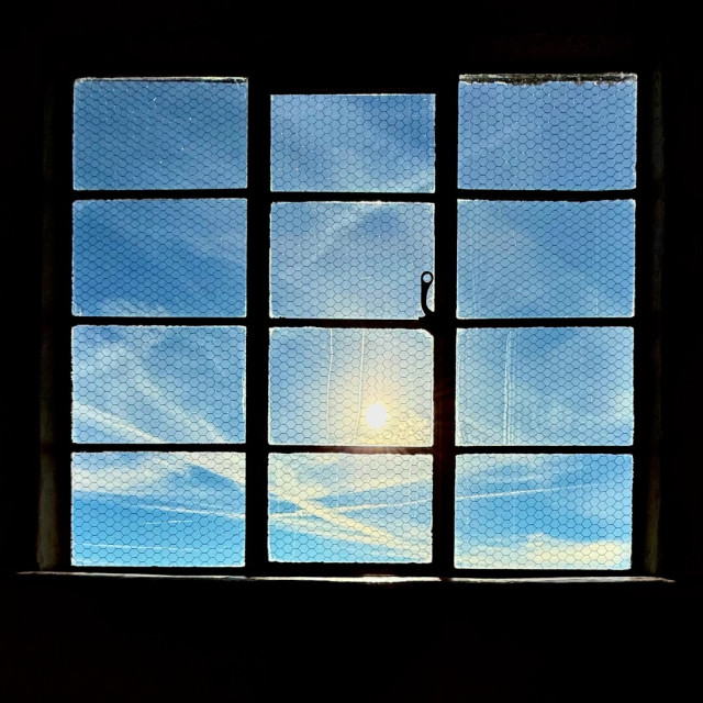 Window in a dark room looking out on a blue sky with wispy clouds