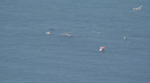 Integrity with four boats immediately nearby, floating in the ocean, helium-filled balloons all deployed to help keep the Integrity capsule right-side up.