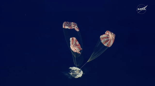 Integrity properly oriented in water as it hits, three parachutes falling to the right and deflating.