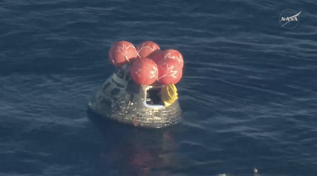 the integrity space capsule floating on the ocean with the hatch now open and a yellow cover of some kind on the door