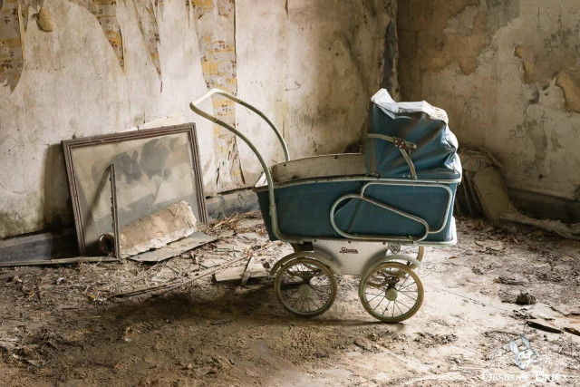 A vintage blue baby pram sits in a dusty, abandoned farmhouse. Peeling walls and a leaning framed photo are visible.A vintage blue baby pram sits in a dusty, abandoned farmhouse. Peeling walls and a leaning framed photo are visible.