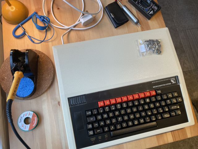 A BBC Micro B on a kitchen table by a soldering iron, a solder sucker, and a few other items.