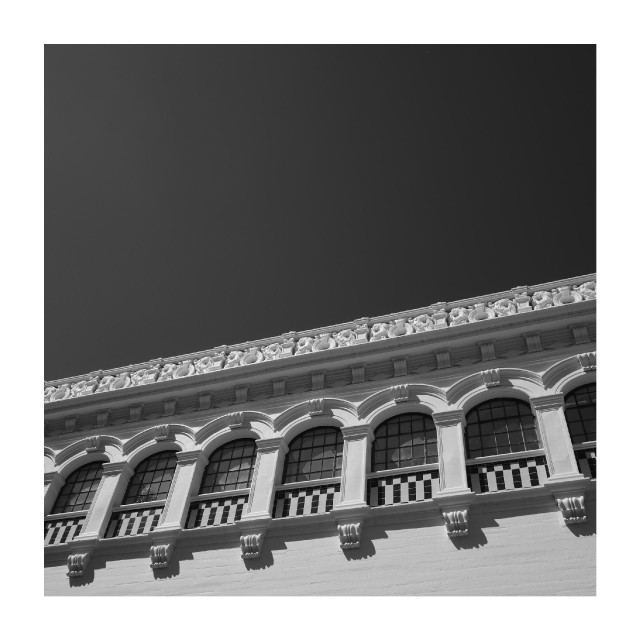 An ornate row of arched windows and decorative molding lines the upper facade of a building against a dark sky.