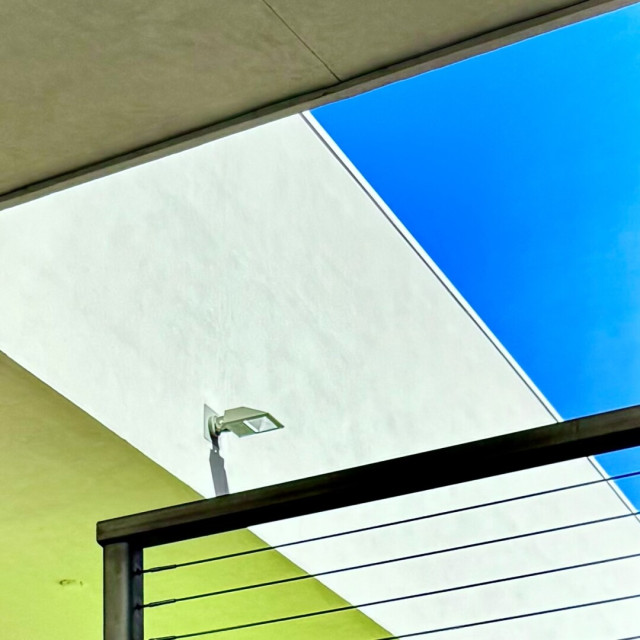 Upward somewhat abstract shot of a white and lime-ish green building with a bright blue sky above.