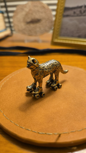 a brass figurine, about five cm long and three cm tall, of a cat on roller skates. it's even wearing a tiny little helmet. for safety!