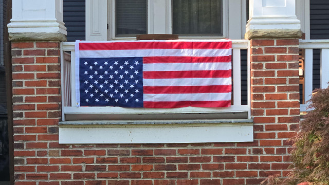 'old glory' hanging upsidedown from the porch of a brick house.
