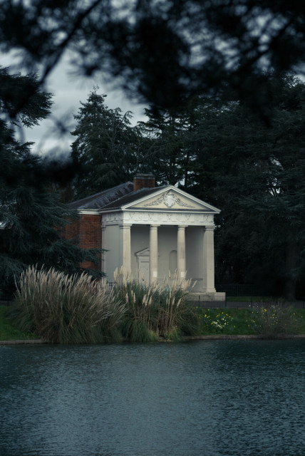 Ruffled blue water, feathered rushes, dark trees, surround a brick building from which sprouts a porch that wants to be a ancient marble temple.