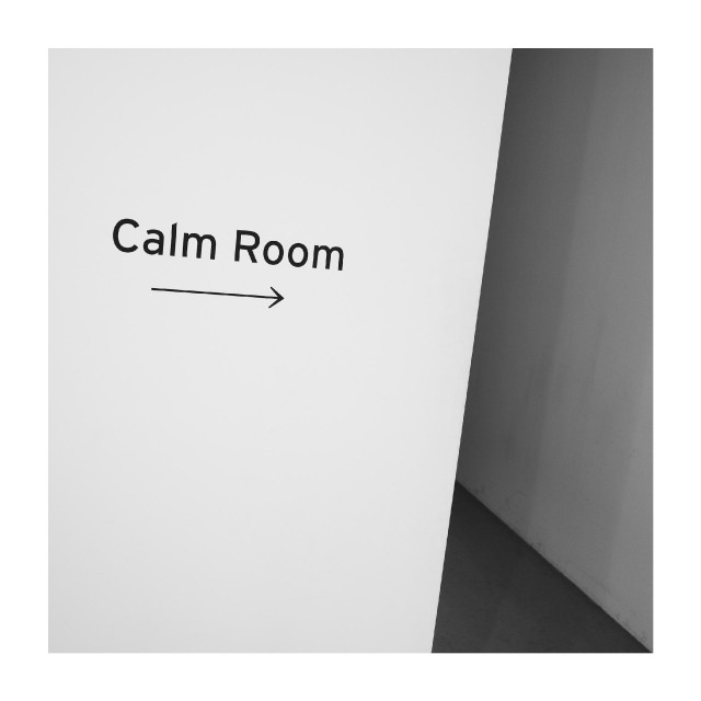 A minimalist wall sign reading “Calm Room” with an arrow points toward a doorway around the corner.