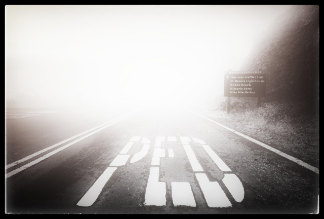 A wide-angle view of a paved roadway at the top of the Marin Headlands. In the foreground: giant white letters on the asphalt spelling PED, part of a ped xing marker. In the distance: fog. White-out levels of fog. 

The fog wasn't that thick in reality... but when you set your ISO too high and your camera maxes out its shutter speed trying to cut the light... well you end up with a hot mess.

"Art," he claimed later.